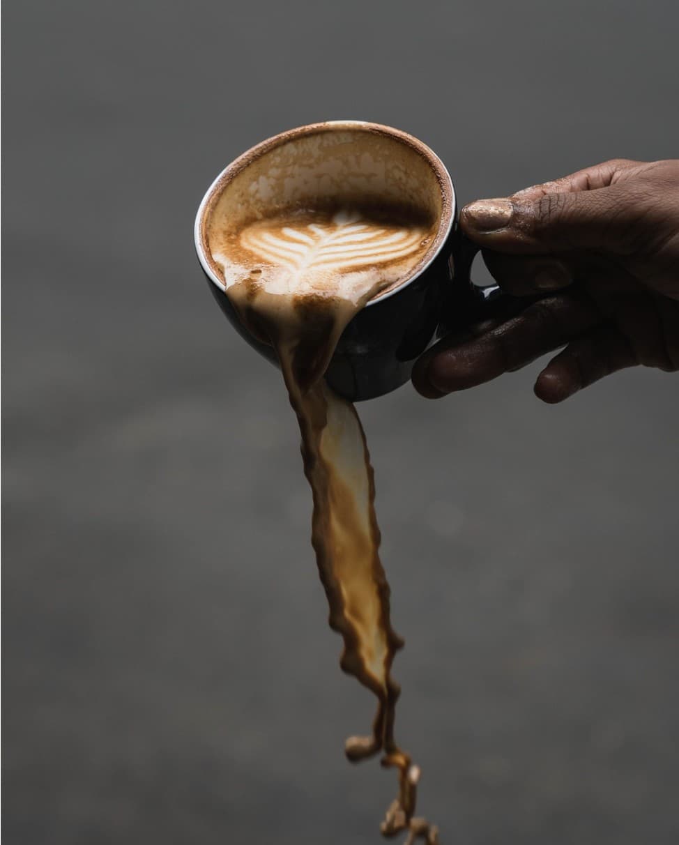 Latte art poured from height into a dark ceramic cup